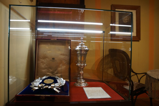 Fragment ekspozycji, tzw. pokój Jana Dzierżona (widoczne meble: sekretarzyk, fotel), na pierwszym planie gablota z nowymi zabytkami: pucharem, wieńcem i listem.
